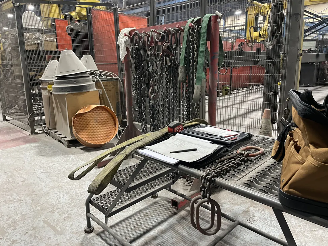 An inspection in progress: completed inspection sheets on a clipboard beside a rack of tagged chain slings and web slings