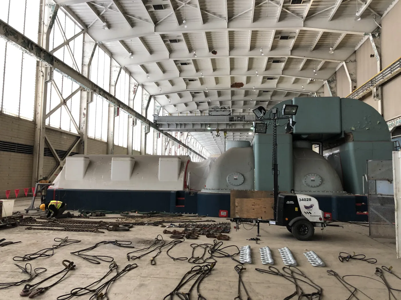 A single inspector working through several hundred chain slings, wire rope slings and shackles laid out across a turbine hall floor