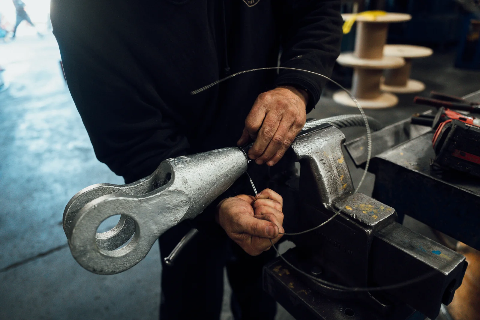A technician winding seizing wire onto a wire rope at the neck of an open spelter socket, held in a bench vise